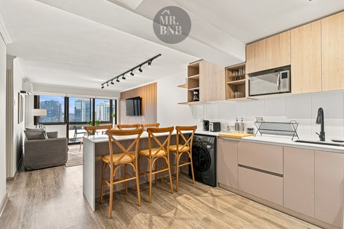 Cocina integrada al living, con isla barra, sillas altas de madera y living al fondo.