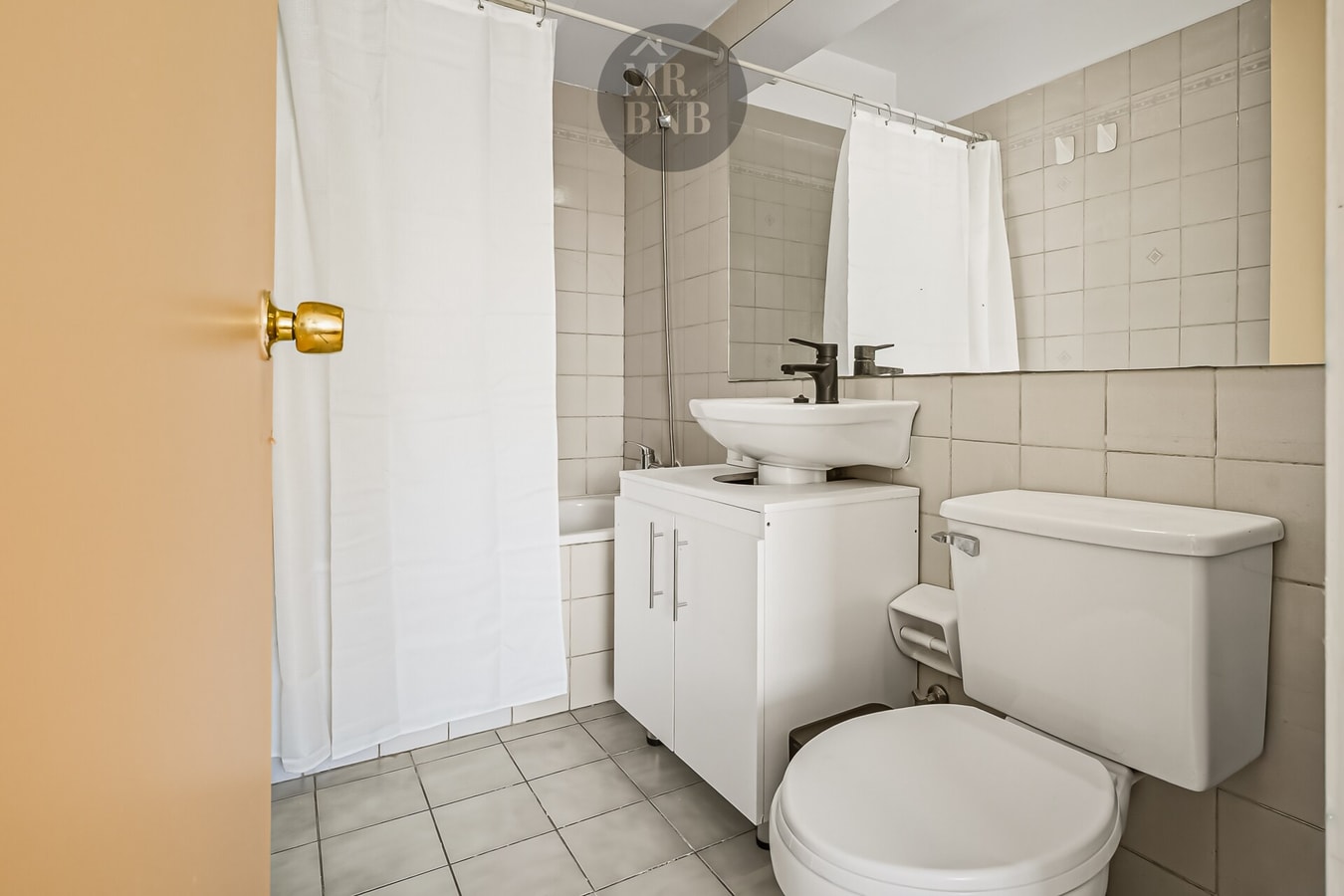 Baño en tonos beige con tina, lavamanos sobre mueble e inodoro