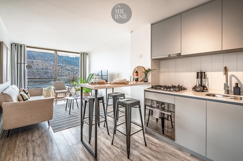 Cocina abierta con barra desayunador, muebles claros y vista hacia el living y la terraza con luz natural