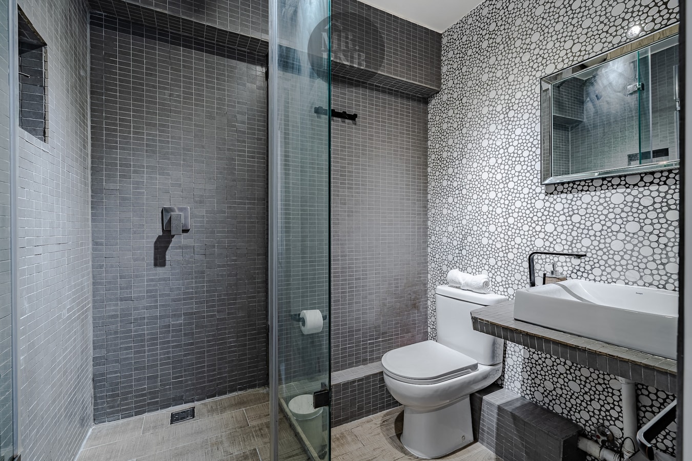 Baño de suite con mosaico gris y ducha de vidrio