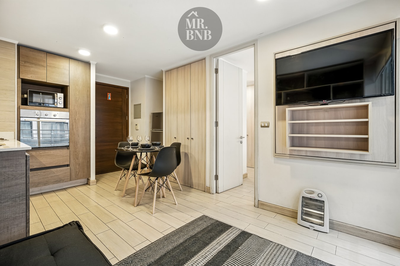 Living con sofá negro, mesa de comedor, televisor y calefactor eléctrico.
