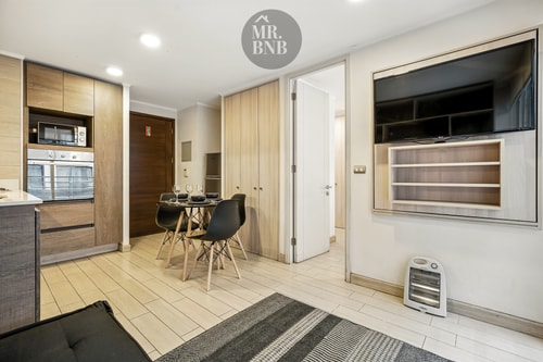 Living con sofá negro, mesa de comedor, televisor y calefactor eléctrico.