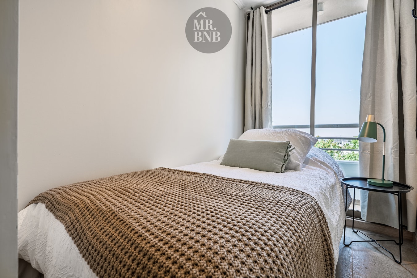 Dormitorio con cama individual, manta café y velador con lámpara