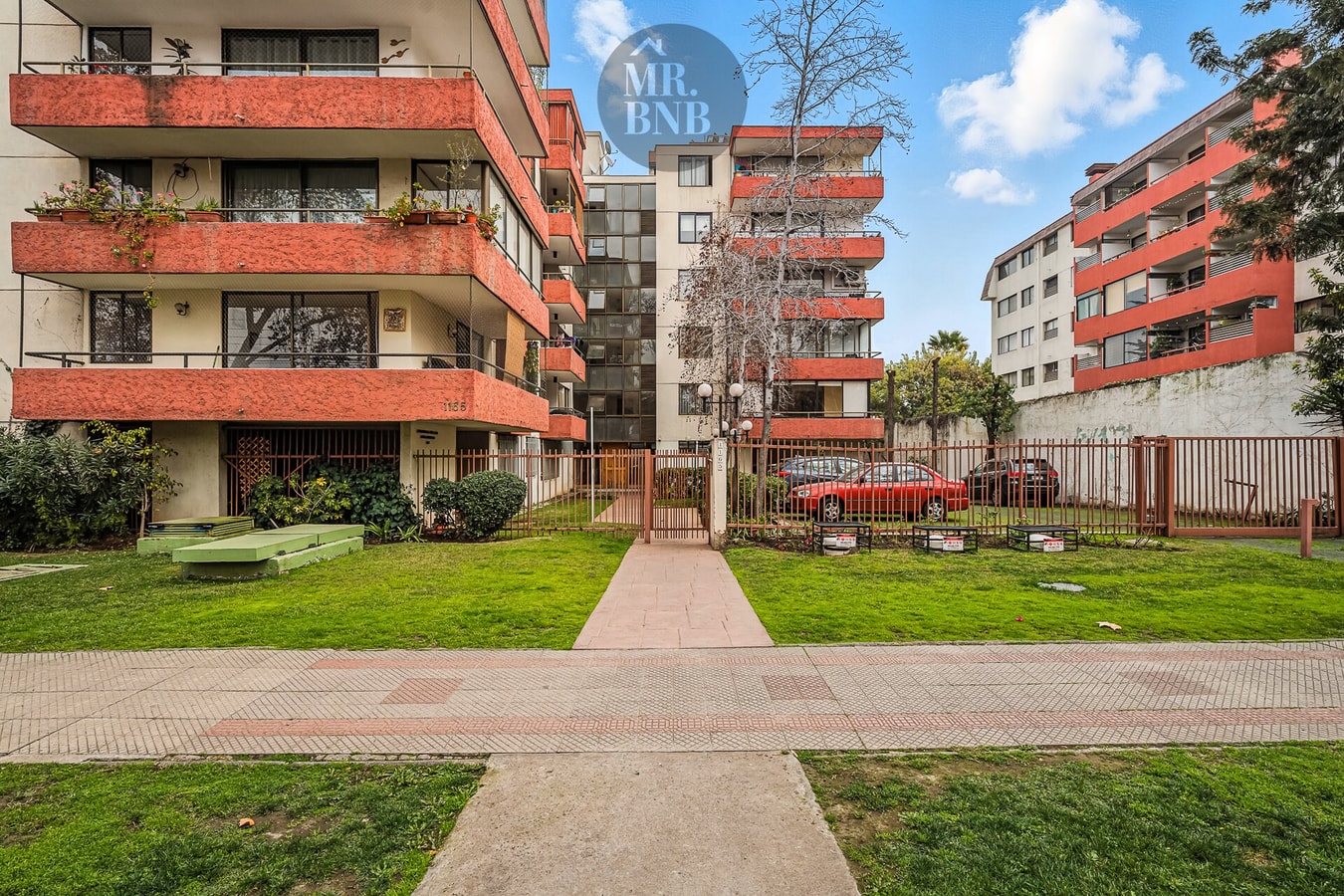 Fachada del edificio con jardín, acceso peatonal y estacionamientos visitas