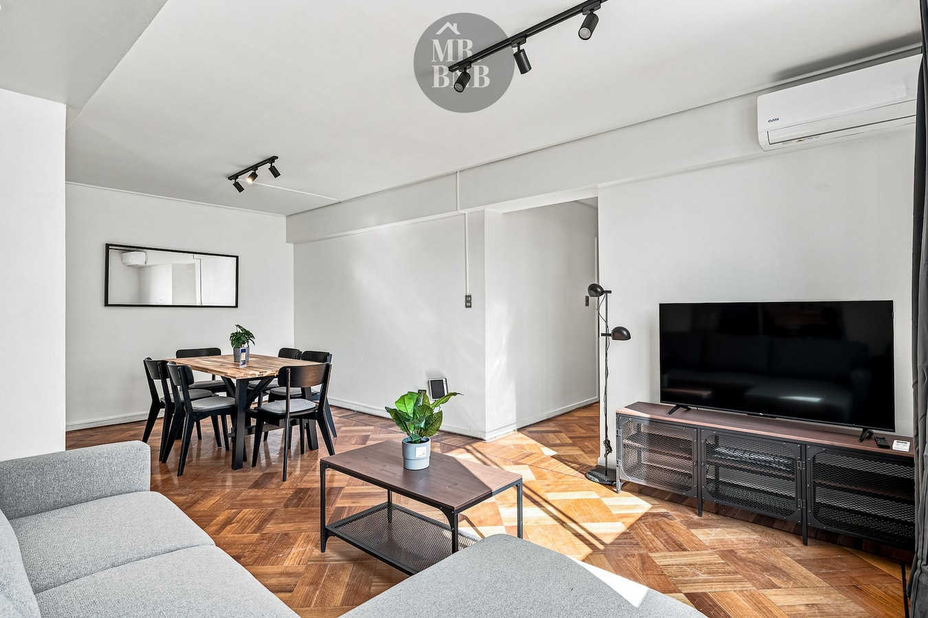 Living comedor con sofá, mesa con sillas, TV sobre mueble y espejo