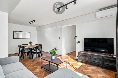 Living comedor con sofá, mesa con sillas, TV sobre mueble y espejo