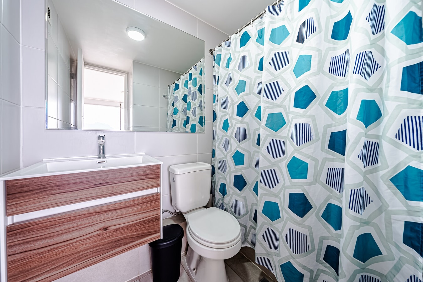 Baño con cortina geométrica azul, mueble vanitorio de madera y WC