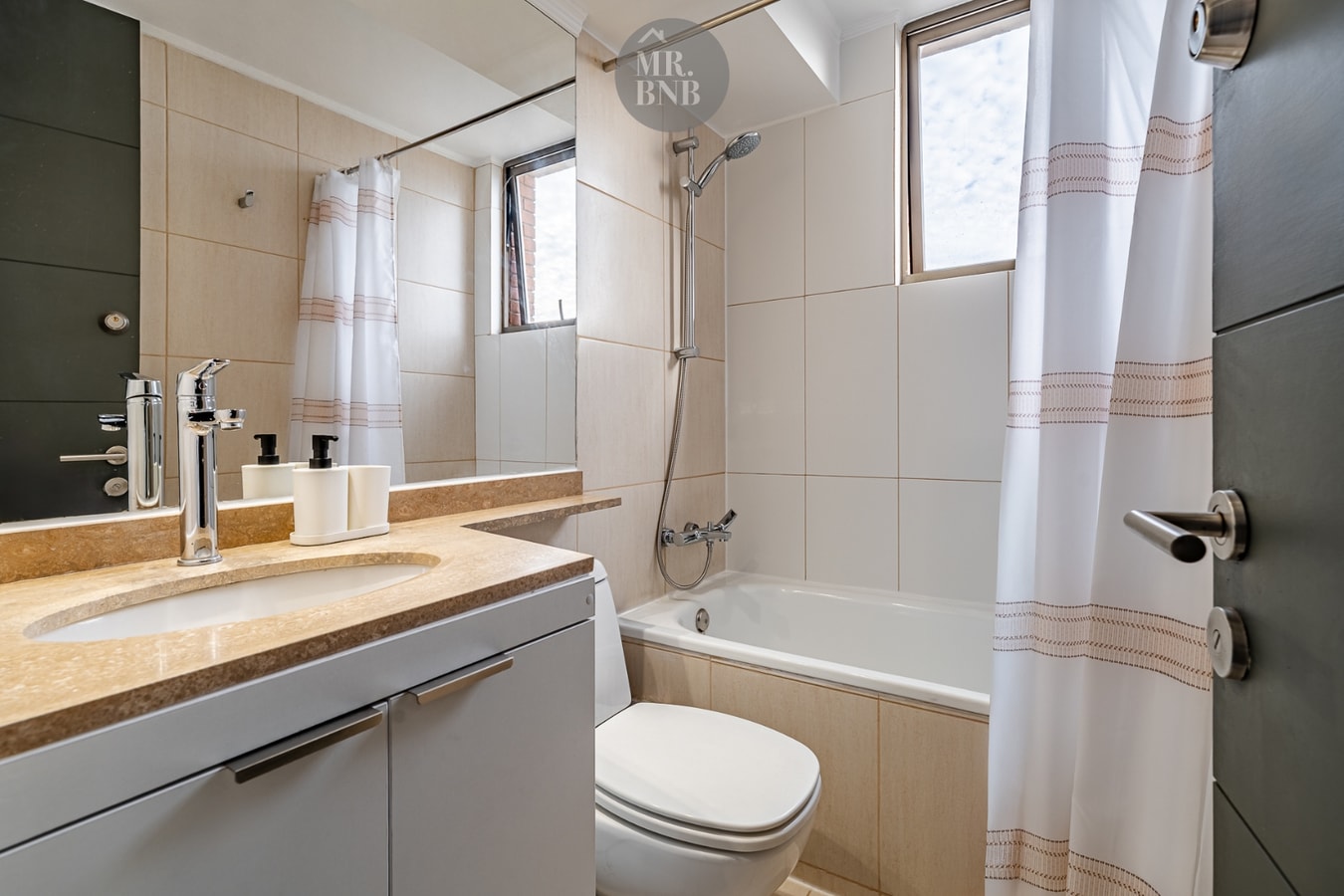 Baño con tina, cortina a rayas, lavamanos de mármol con dos llaves y ventana con luz natural