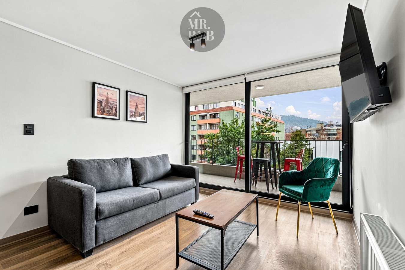 Living comedor con sofá gris, mesa de centro, silla verde y ventanal con vista a la calle