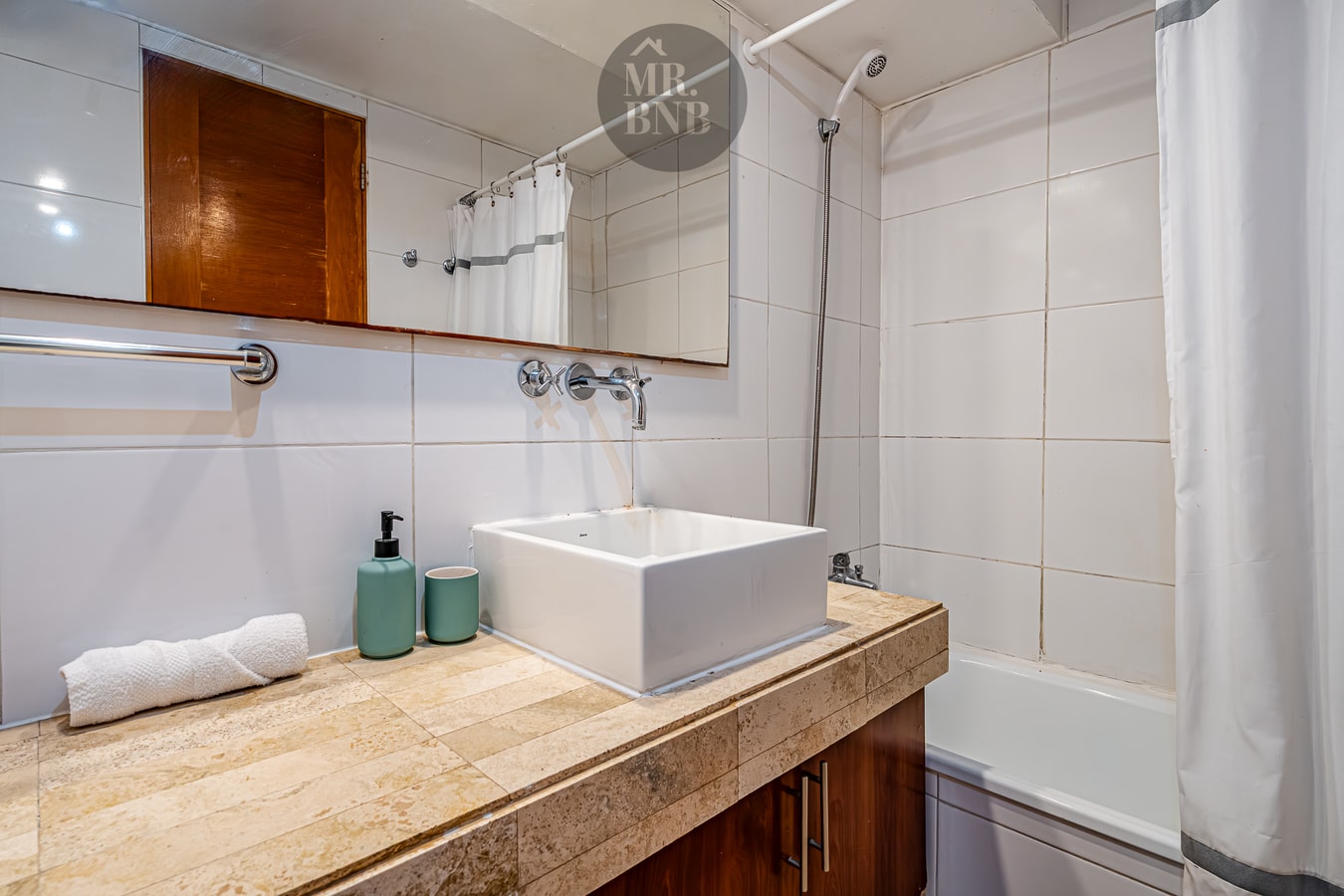 Detalle de lavamanos con toallas y amenities, mueble de madera y tina al fondo