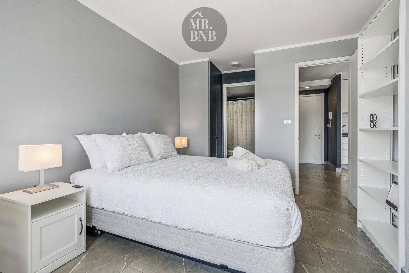 Dormitorio con cama, veladores, repisas y vista al pasillo