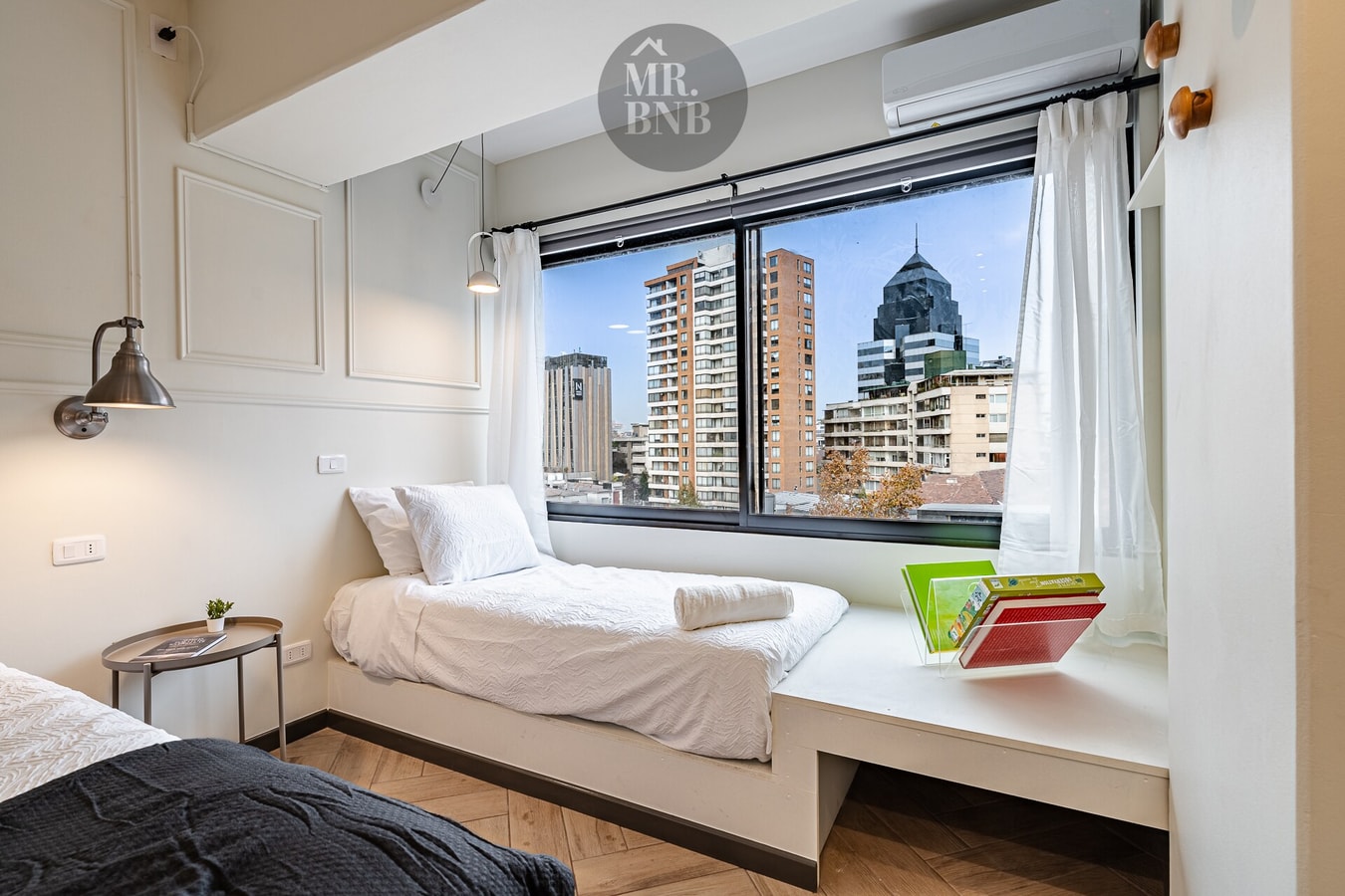 Dormitorio con cama, ventanal con vista a edificios y mural de la ciudad
