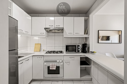 Cocina blanca en L con horno, cocina a gas y muebles altos.