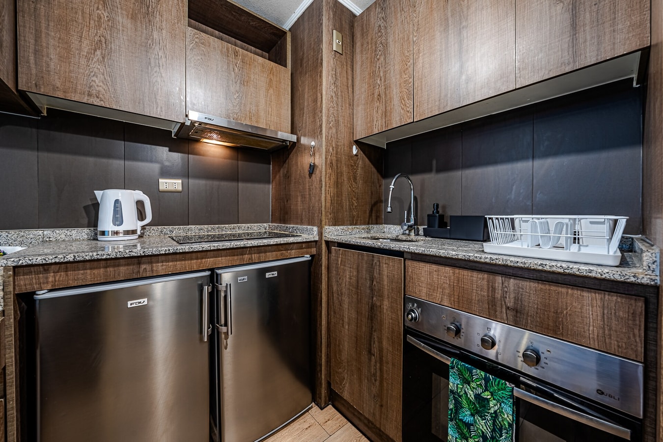 Cocina con muebles oscuros, hervidor, refrigerador y horno
