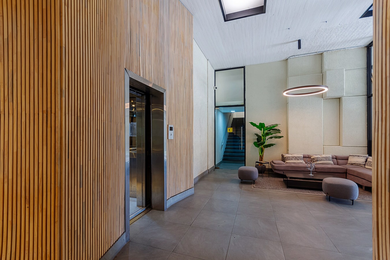 Hall de acceso del edificio con revestimiento de madera, ascensor, lámpara circular y sofá de espera