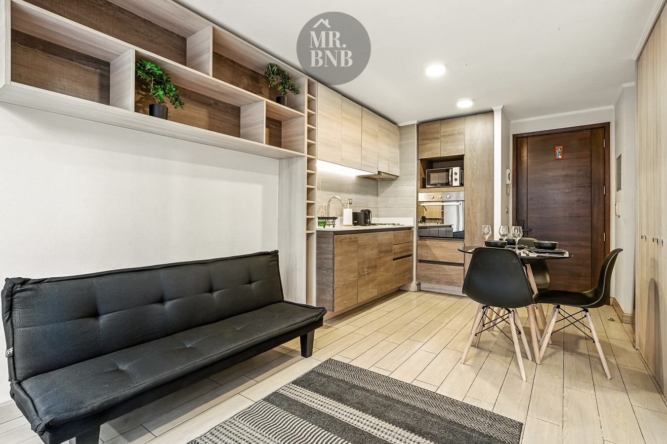 Living con sofá cama negro, mesa de comedor y cocina al fondo.