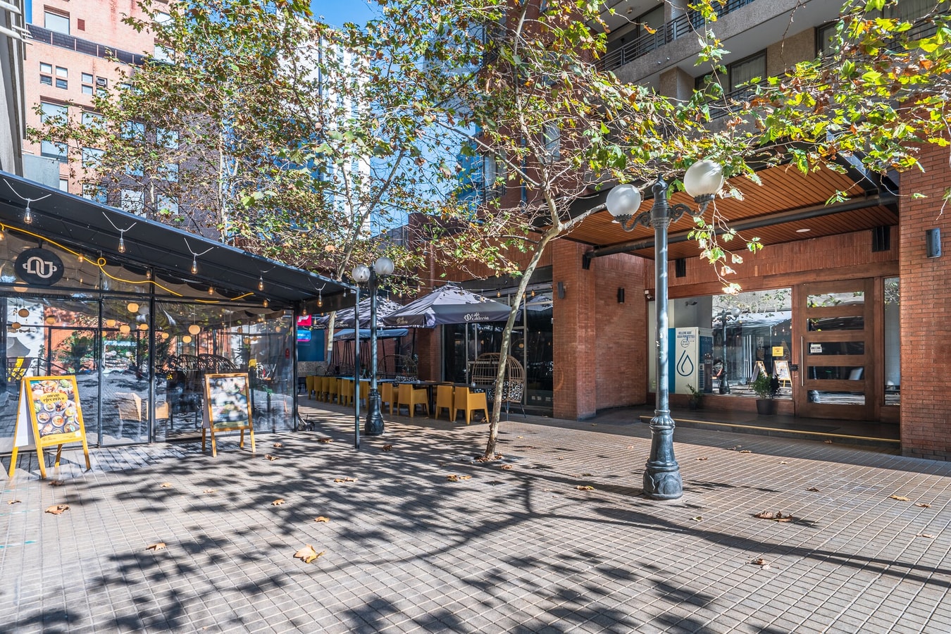 Calle peatonal arbolada con locales comerciales y mesas exteriores, propia del barrio