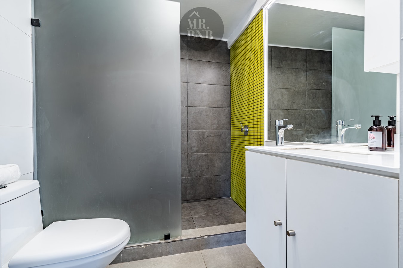 Baño con ducha de vidrio esmerilado y mueble vanitorio con azulejo amarillo
