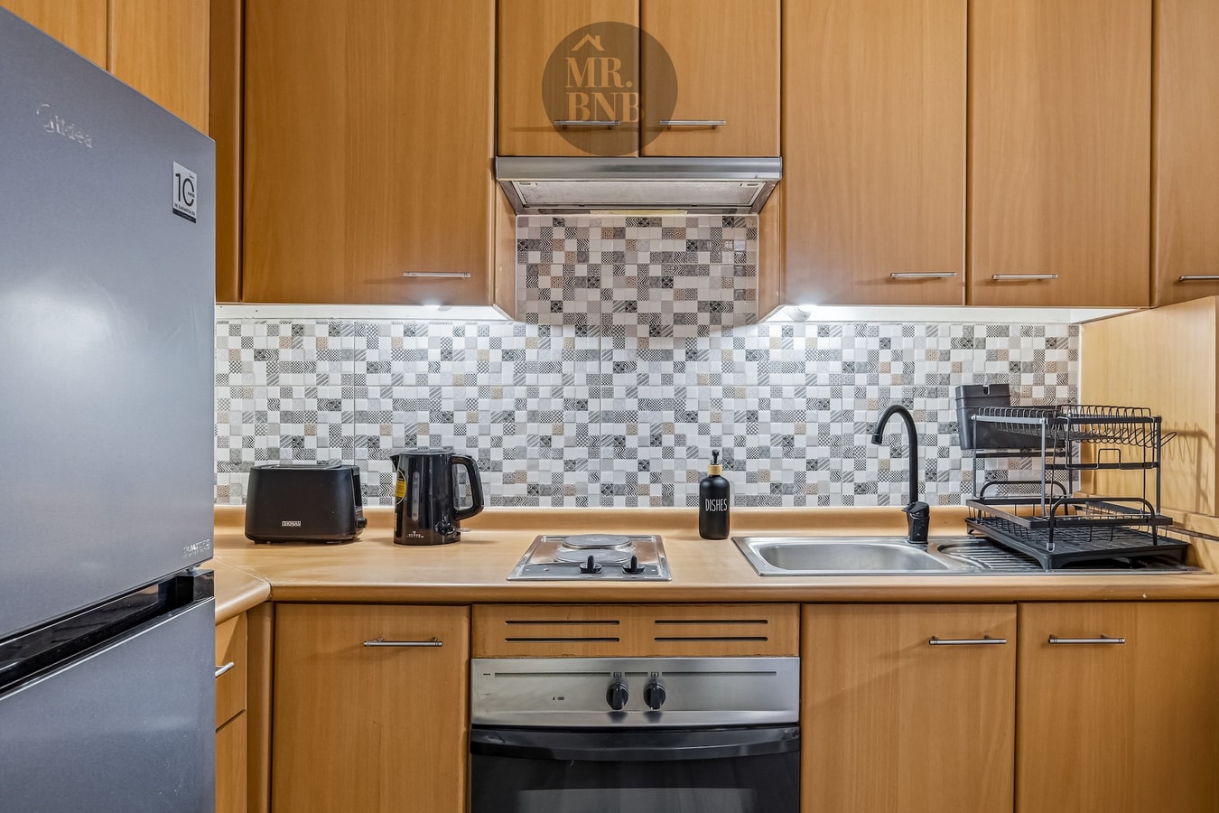 Cocina con muebles de madera, encimera a gas, campana y refrigerador