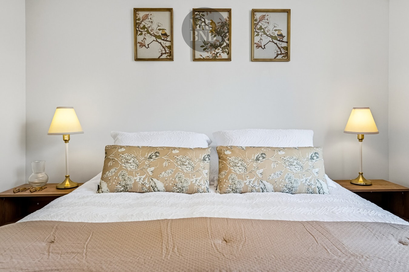 Dormitorio con cama matrimonial, veladores con lámparas y cuadros decorativos sobre el respaldo