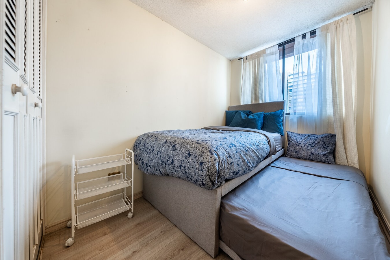 Dormitorio con dos camas individuales, una de ellas tipo carro extraíble, y ventana con persianas.