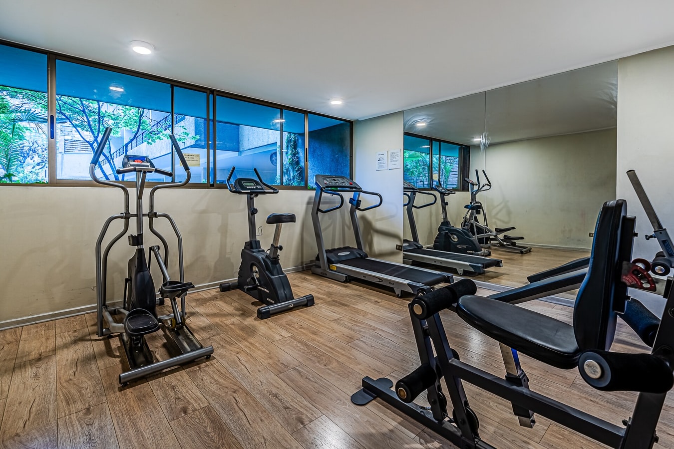 Gimnasio con trotadoras, bicicletas estáticas y espejo de pared
