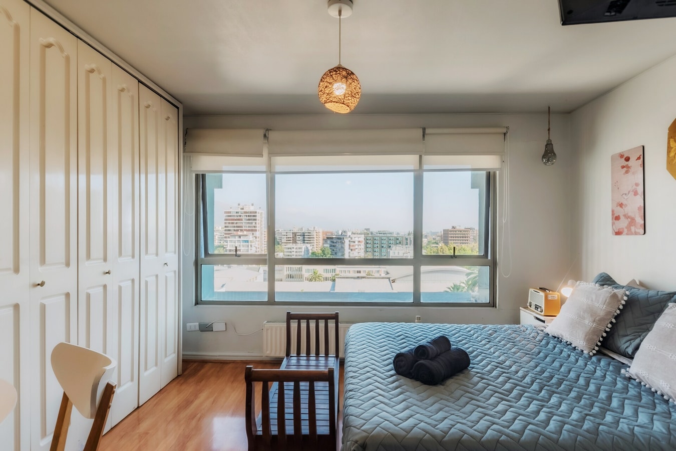 Estudio con cama junto a ventanal amplio con vista a la calle, closet blanco
