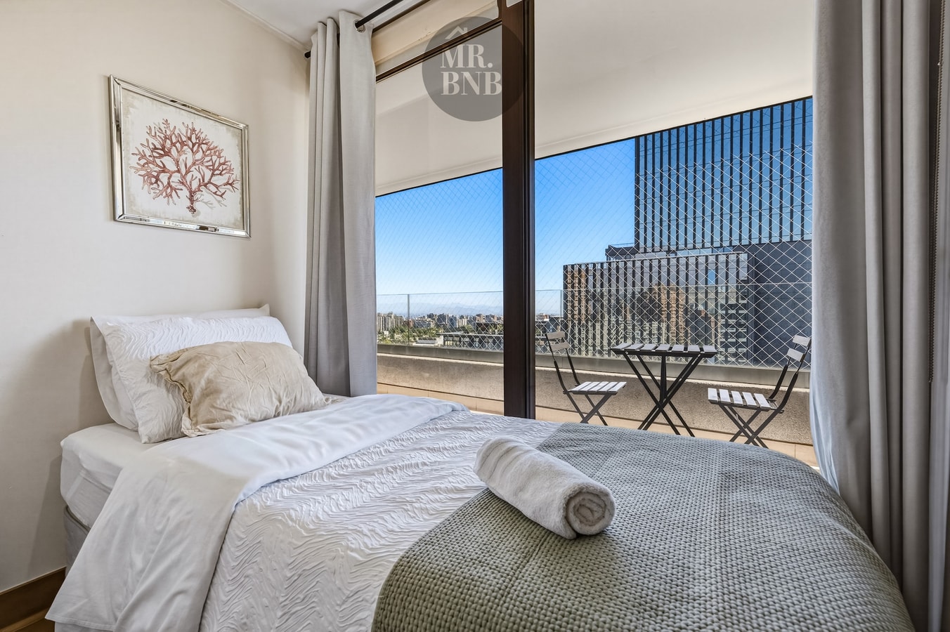 Dormitorio con cama y vista a la ciudad a través de ventanal con cortinas.