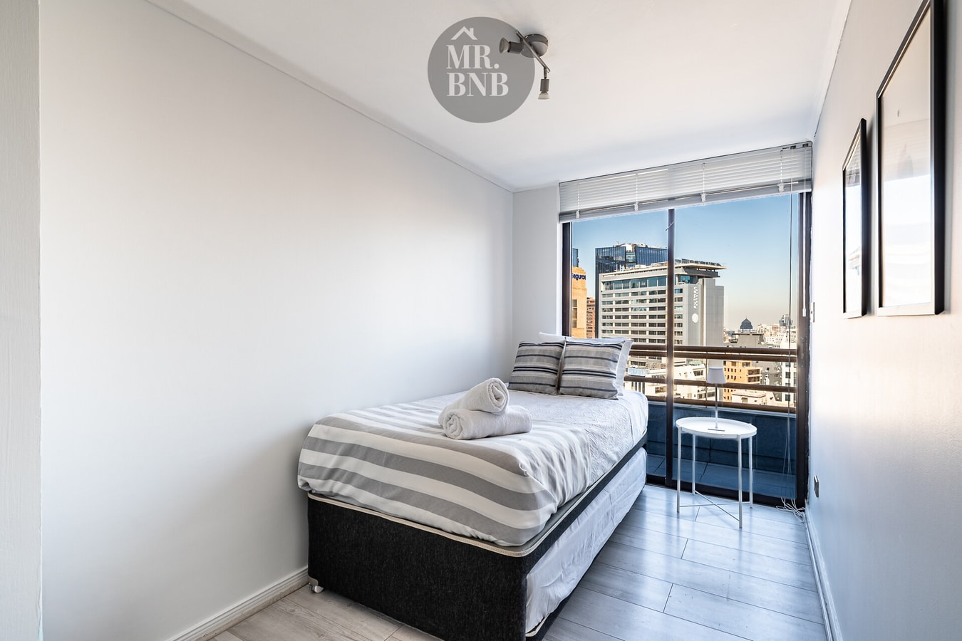 Dormitorio con cama individual y ventanal con vista a edificios