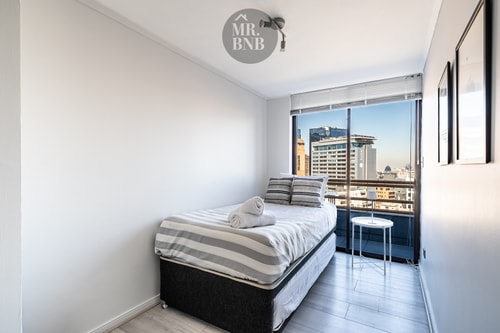 Dormitorio con cama individual y ventanal con vista a edificios