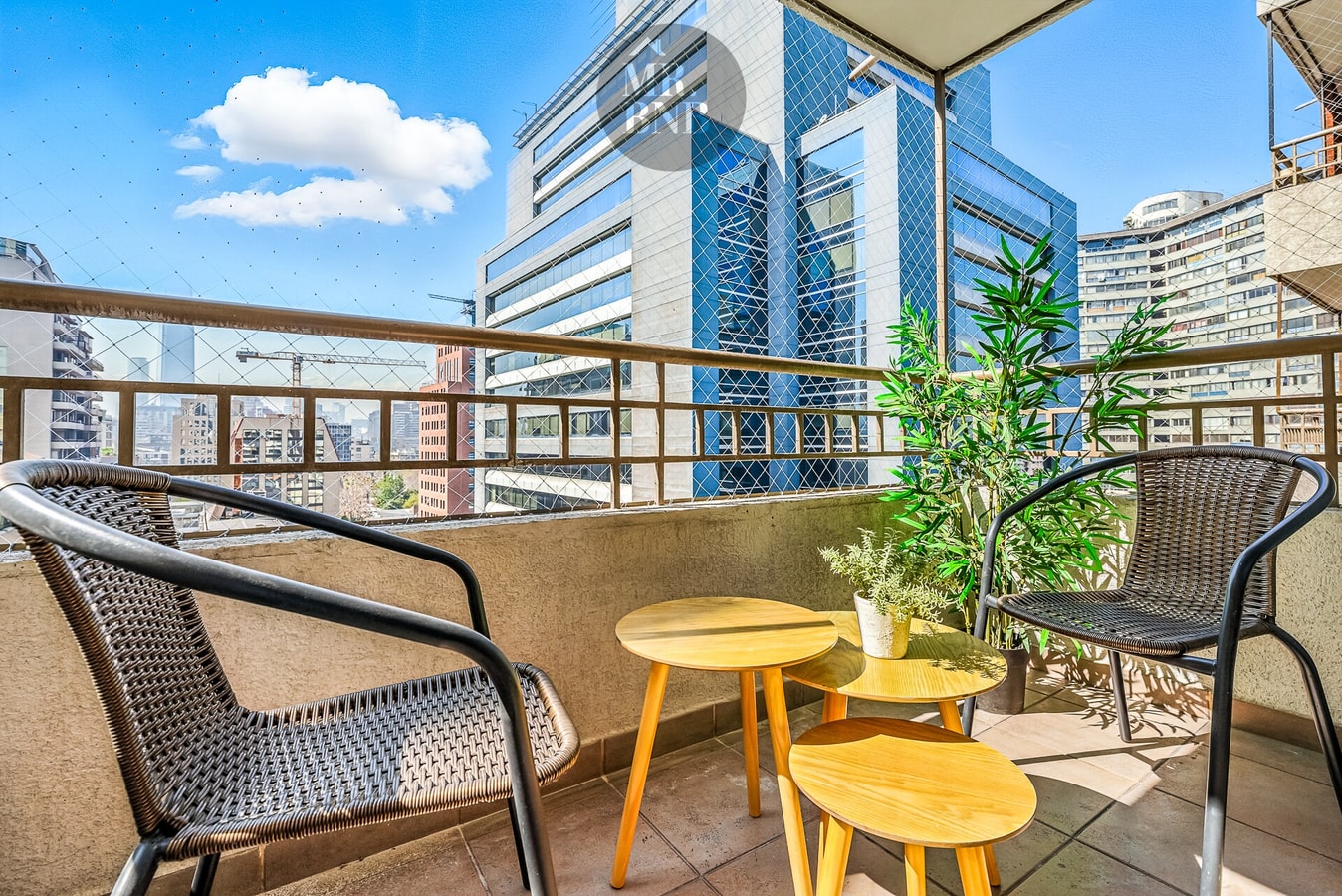 Terraza con sillas, mesas auxiliares y plantas, con vista a los edificios del entorno.