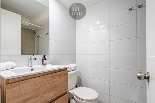 Baño con lavamanos de madera, inodoro y ducha con puerta de vidrio.