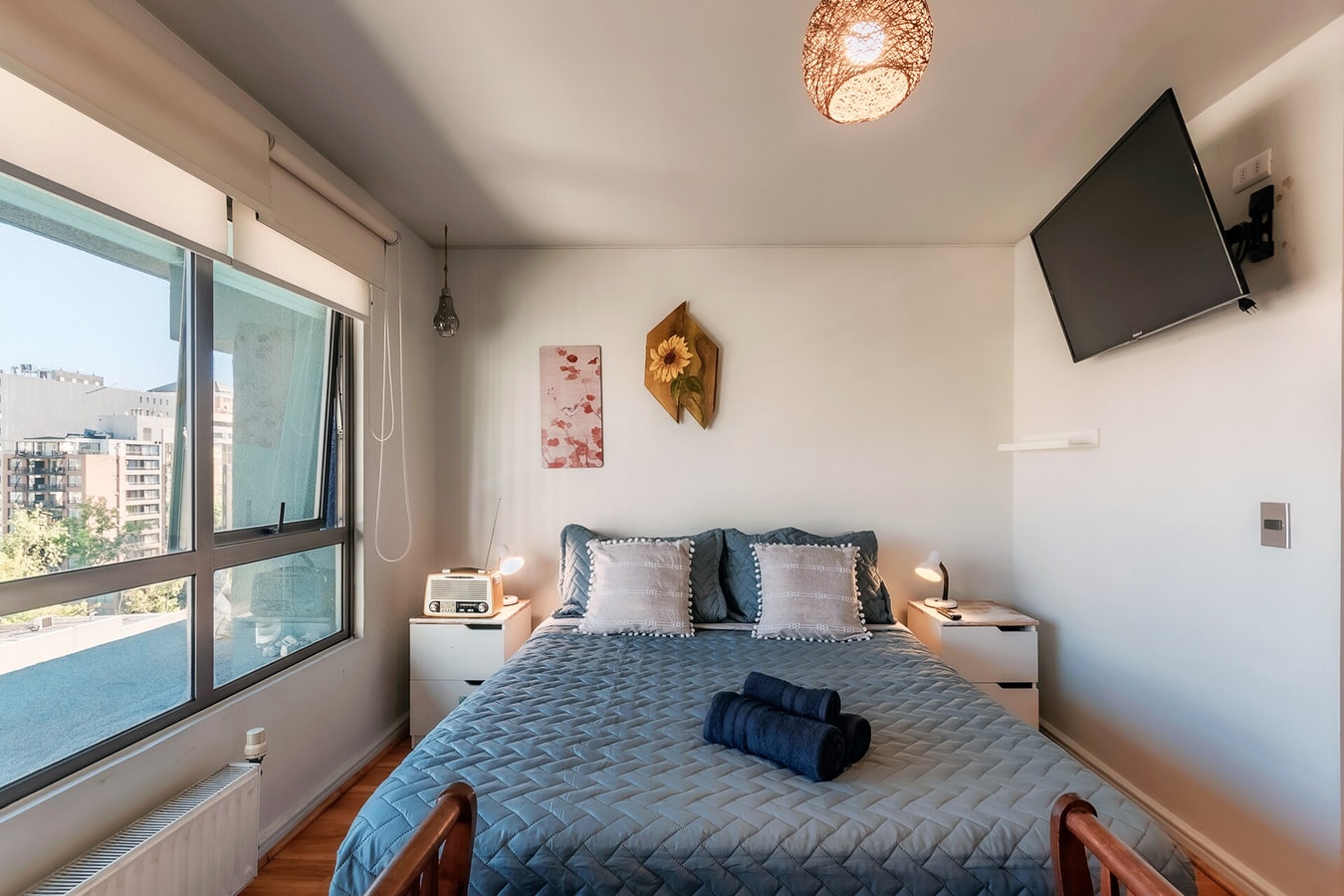 Estudio con cama junto a ventanal, televisor en la pared y veladores