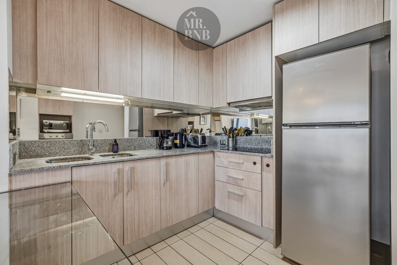 Cocina con muebles de madera clara, refrigerador de acero inoxidable y mesón con lavaplatos.