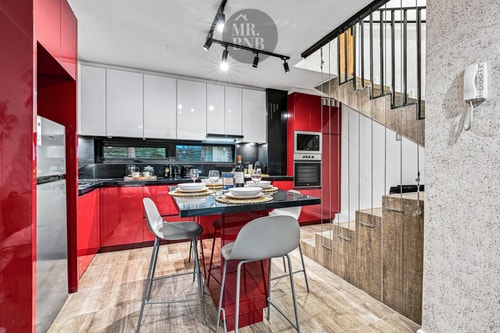 Cocina de muebles rojos brillantes con barra alta, sillas y escalera hacia el segundo nivel