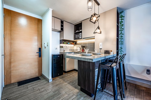 Cocina y living con vista a la puerta de entrada de madera, barra con banquetas y estante decorativo al fondo