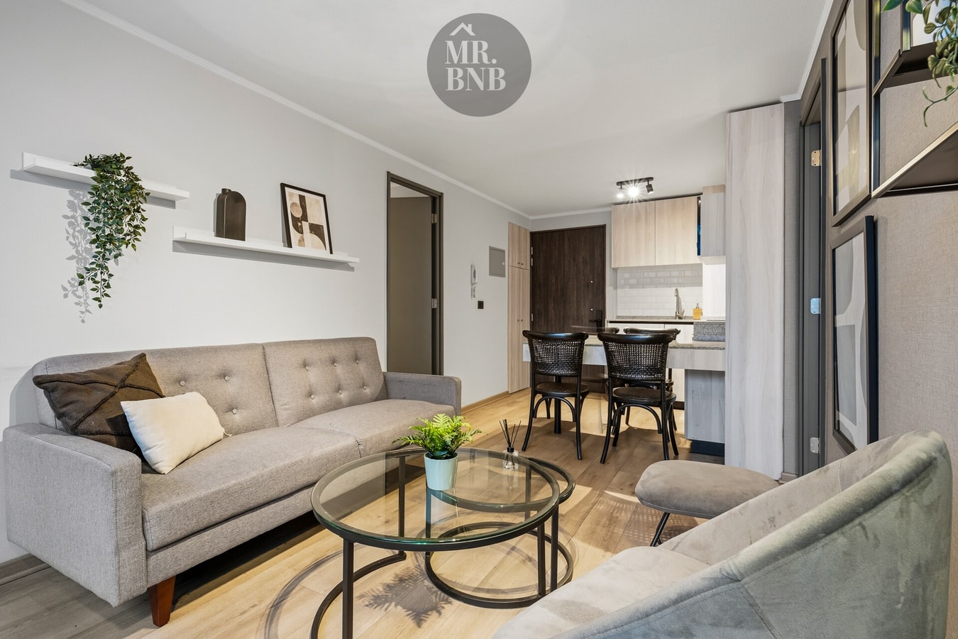 Living con sofá gris, cojines, repisa con plantas y comedor al fondo