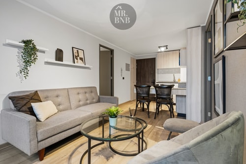 Living con sofá gris, cojines, repisa con plantas y comedor al fondo