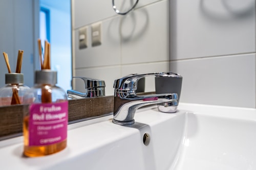 Detalle del lavamanos del baño con grifería cromada y productos de cortesía sobre el mesón