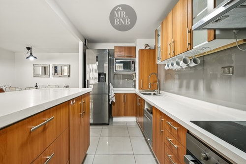 Cocina en L con isla blanca, campana y muebles de madera