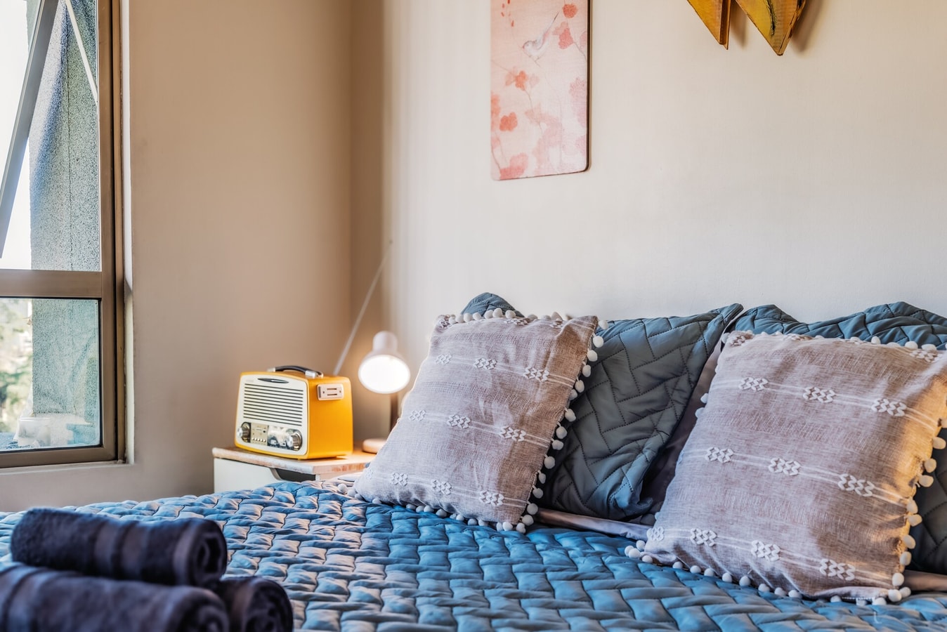 Detalle de toallas enrolladas sobre la cama junto a un velador con lámpara