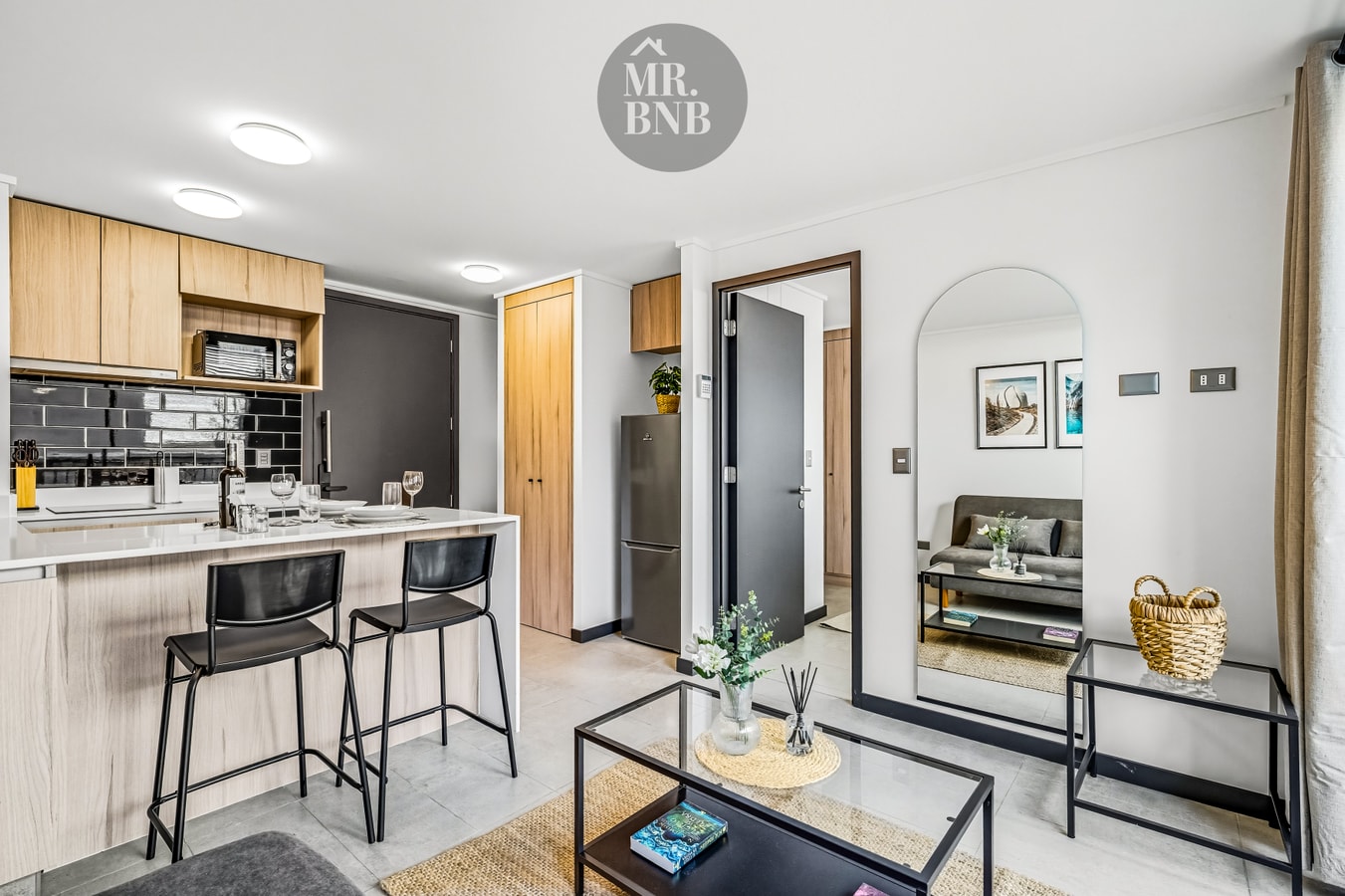 Living con mesa de centro y espejo de arco, la cocina con barra al fondo y el refrigerador junto al pasillo de entrada