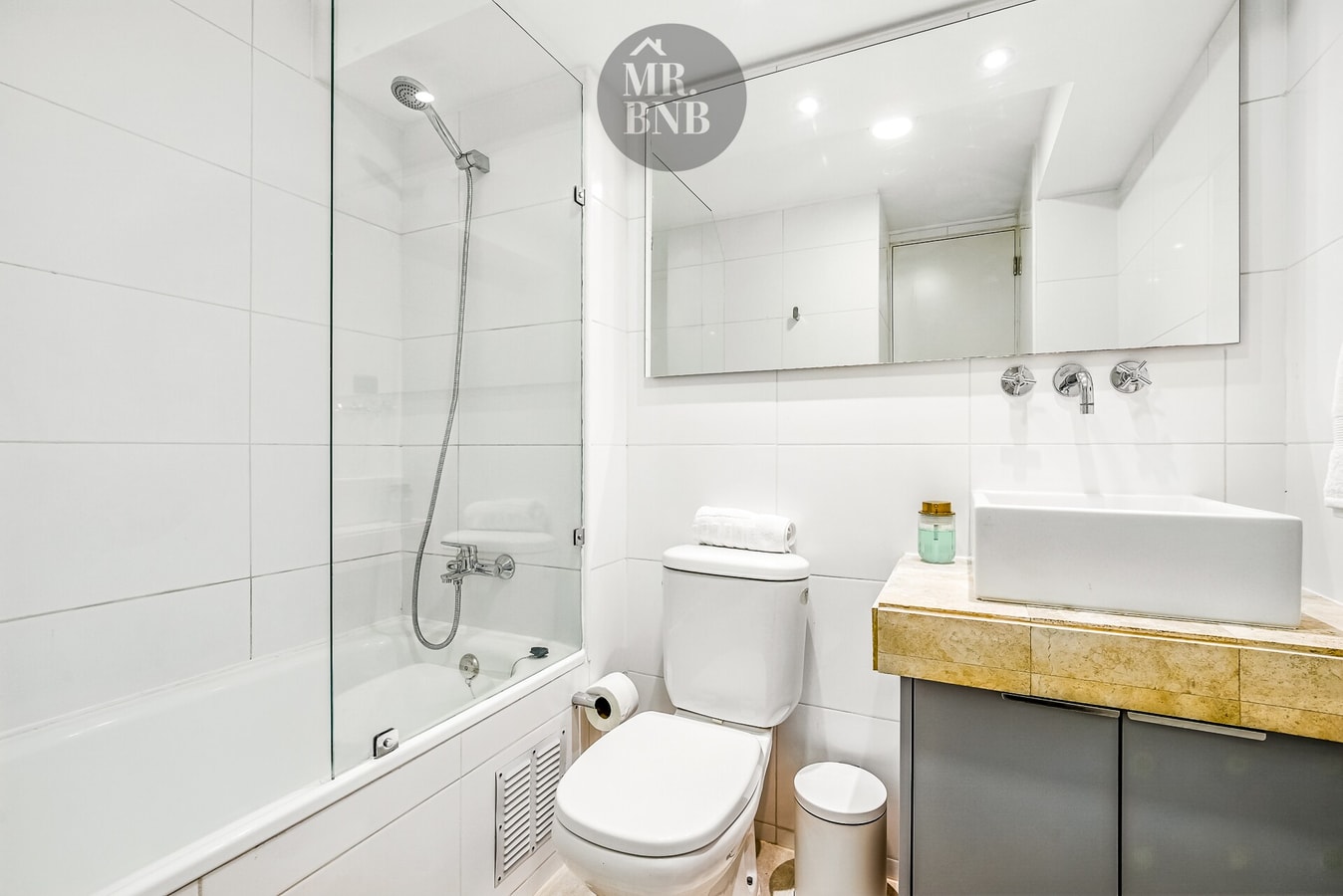 Baño con tina, ducha, inodoro y lavamanos bajo espejo amplio.