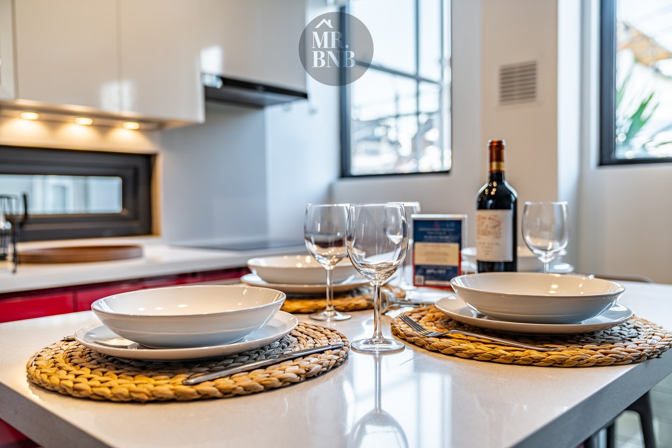 Mesa puesta con copas de vino, platos y ventanas al fondo
