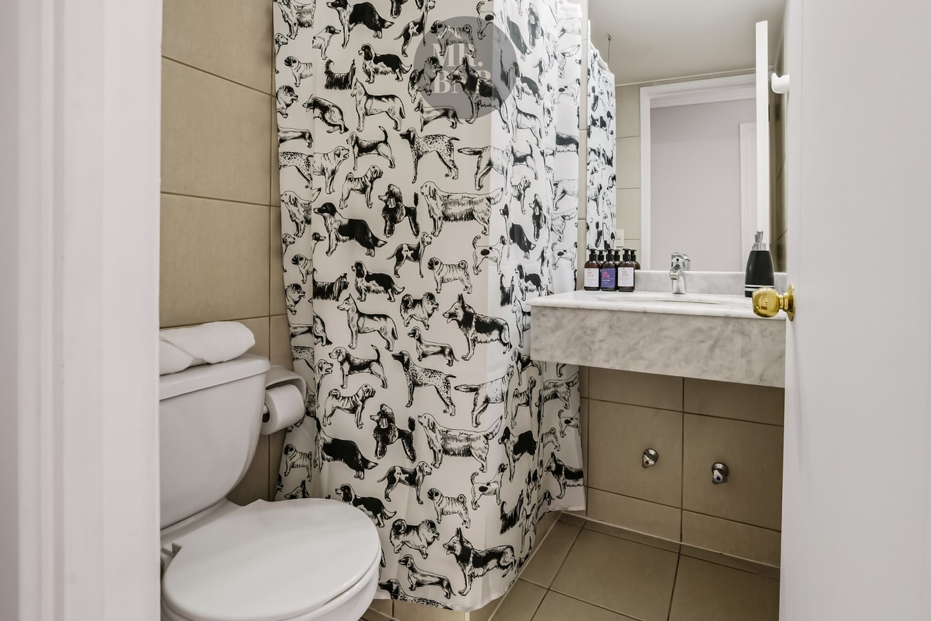 Baño con cortina estampada, inodoro, lavamanos de mármol y amenities.