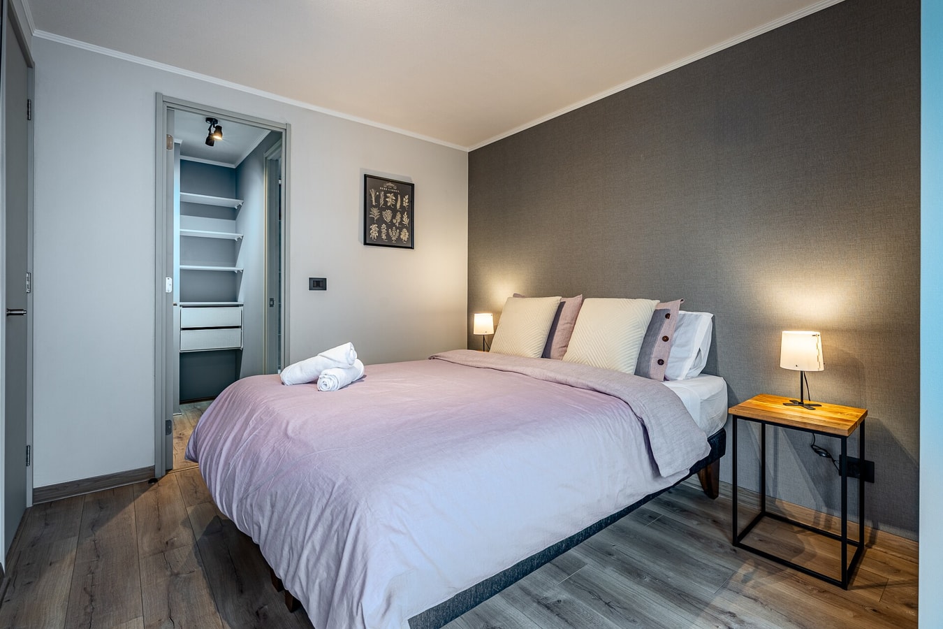 Dormitorio con cama, velador con lámpara y closet abierto al fondo.