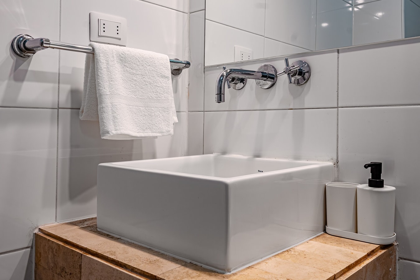 Detalle de baño con lavamanos cuadrado sobre mueble de madera y toallero