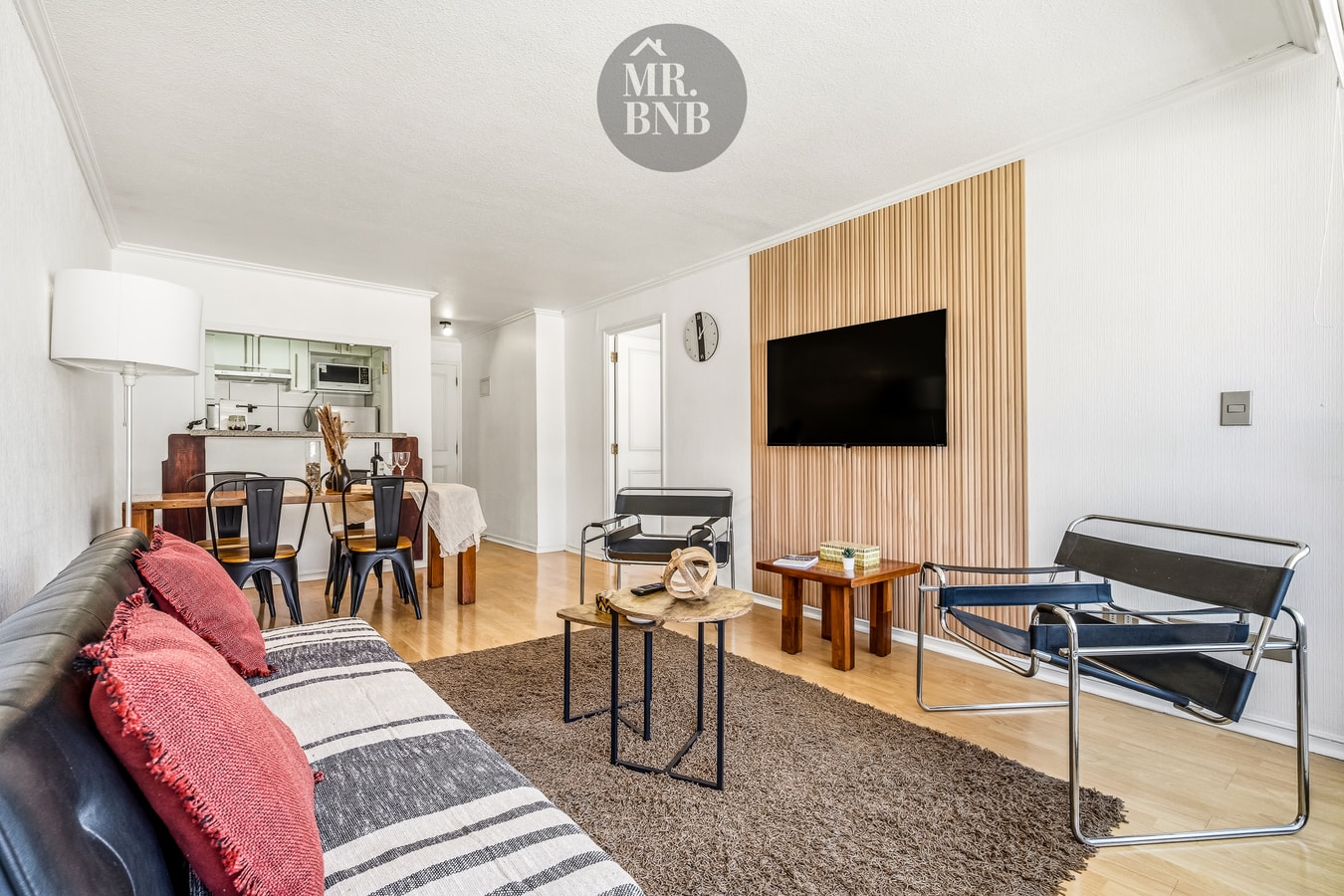 Living con sofá gris con cojines, panel de madera con televisor y sillas de diseño