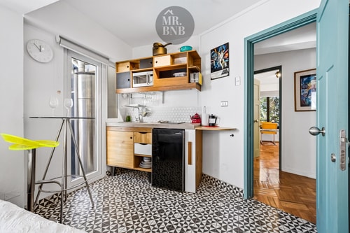 Kitchenette de suite con reloj, repisas de madera y espejo, puerta turquesa de acceso
