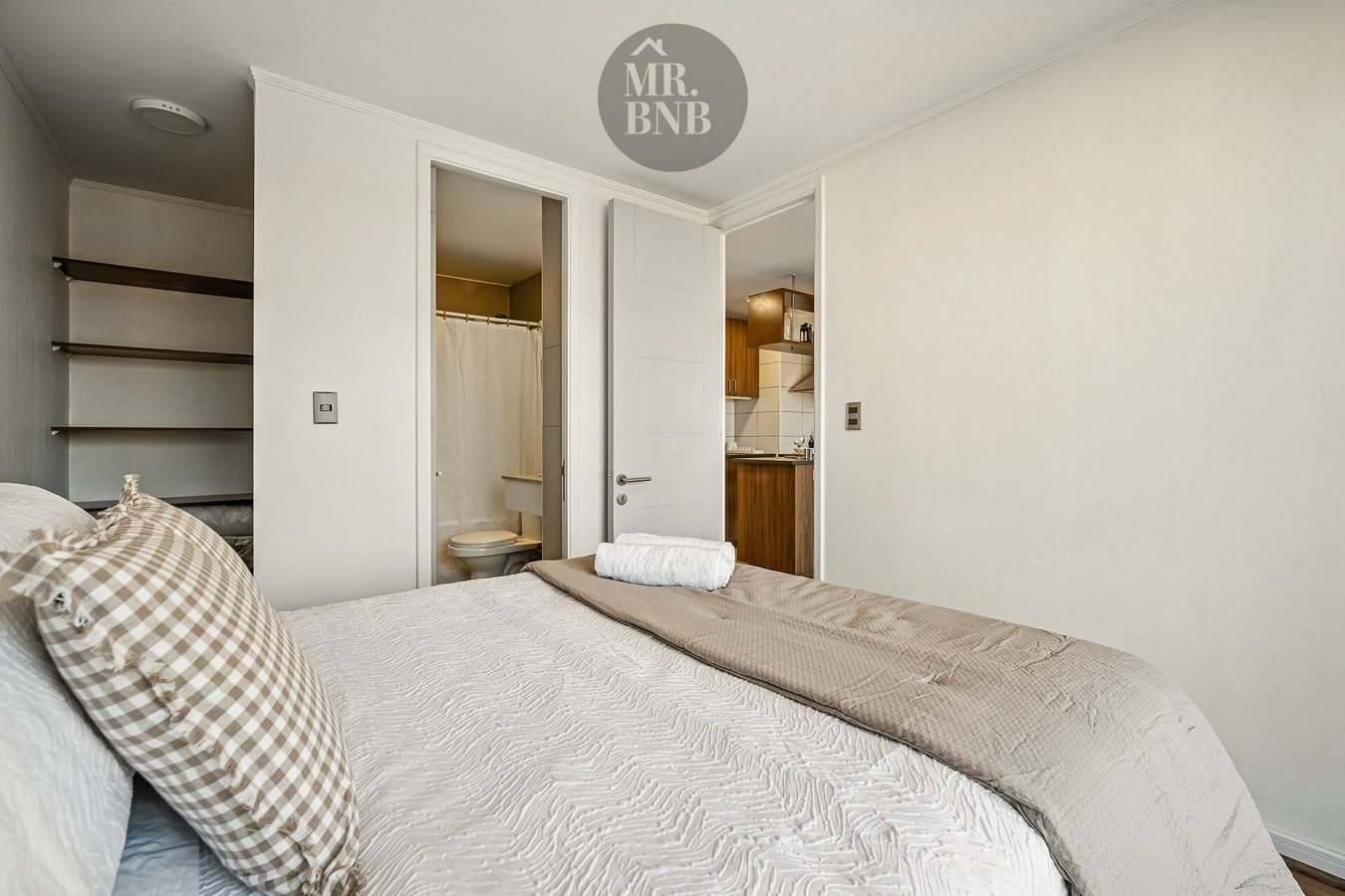 Dormitorio con cama doble, estantería empotrada y puerta hacia baño y cocina